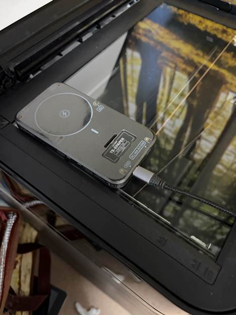 The LilyGo T5 e-paper board lying face-down on a flatbed scanner's glass, USB-C cable running out from under the lid